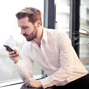 A photo of a man in a white button-down reading a text message.